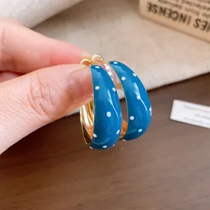 Close-up of retro teal blue enamel hoop earrings with white polka dots and gold finish