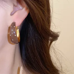 Close-up detail of glossy brown hoop earrings with white polka dots and golden accents.