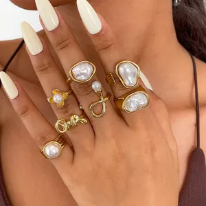 Close-up of a 7-piece retro gold ring set with pearls and flower designs on a hand.