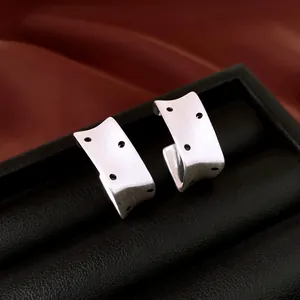 Close-up view of silver square earrings featuring brushed metal and black polka dots