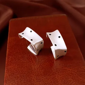 Macro view of silver-tone square earrings with black polka dots and brushed finish