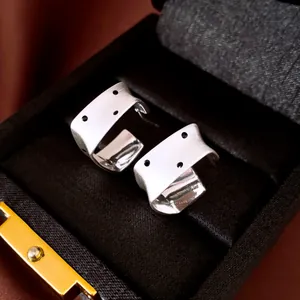 Detail view of silver brushed square stud earrings with black dot patterns in a box.