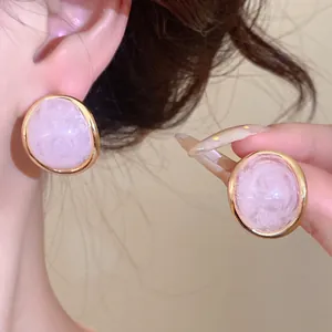Close-up of pink marbled resin oval stud earrings with elegant gold-tone metal frames