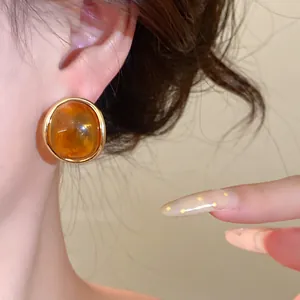 Close-up detail view of a retro amber resin stud earring with gold rim on model ear