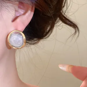 Macro detail of a vintage marbled resin stud earring with gold-tone rim worn on ear