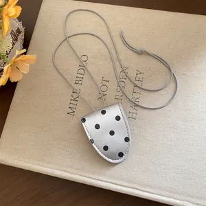 Vue détaillée d'un collier porte-lunettes vintage à pois argentés sur un livre en lin.