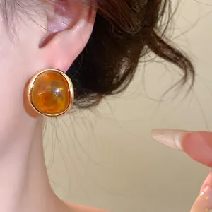 Detailed view of vintage amber resin oval stud earrings with golden trim on female ear