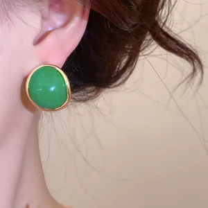Close-up of a vintage-style green resin stud earring with gold border on model ear.