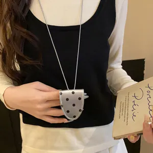 Gros plan d'un collier pince à lunettes à pois rétro porté par un mannequin avec un livre.
