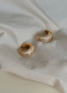 Close-up of elegant vintage gold hoop earrings with white enamel and sparkling zircons
