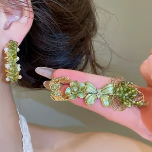 Detail van zilveren oorbellen met groene kristallen bloemen en een elegante vlinder.