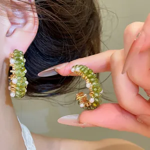 Detailopname van handgemaakte C-vormige oorbellen met groene kristallen en parels