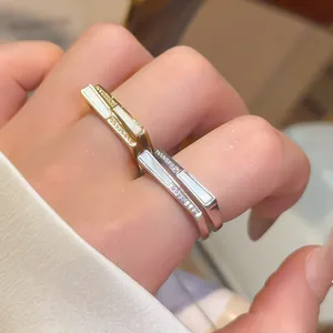 Close-up of gold and silver square rings with zircon and white inlay on finger.