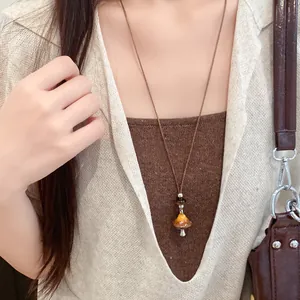 Détail d'un collier vintage en cuir avec un pendentif émaillé en forme de champignon.