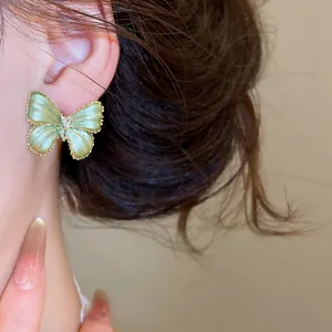 Close-up van een groene vlinder oorknop met zirkonia accenten op het oor van model.