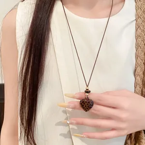 Gros plan du pendentif cœur léopard vintage sur un collier en cordon de cuir marron.