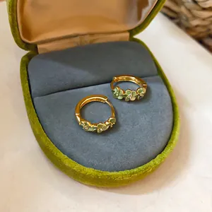 Detail van gouden oorringen met groene bloemen in een luxe groen fluwelen doosje