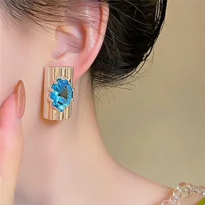 Detailopname van een blauwe zirkoon oorsteker met een gouden geribbelde rechthoek