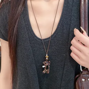 Vue détaillée d'un collier pendentif ours léopard vintage porté sur un gilet sombre.