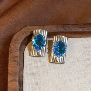 Detailopname van zilveren oorknopjes met ovale blauwe zirkoon en geribbelde textuur
