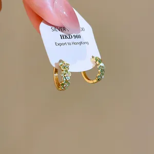 Detailopname van gouden oorringen met groene bloemen en glinsterende zirkoniasteen.