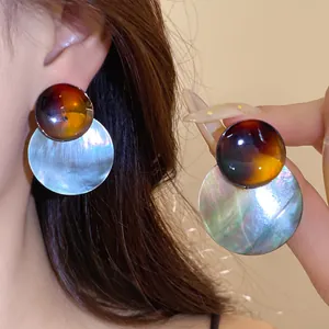 Nahaufnahme von Retro-Ohrringen mit bernsteinfarbenen Acetat-Steckern und Perlmutthängern.