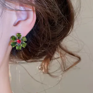 Close-up of green and red flower-shaped cubic zirconia earring worn on an ear.