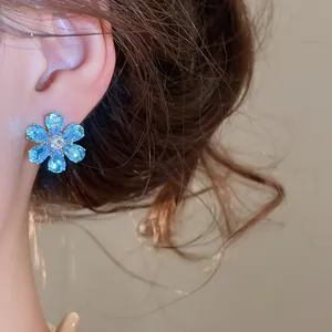Detailed close-up view of a sparkling blue flower zircon stud earring worn on model's ear