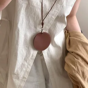 Minimalistische braune Lederschnur-Halskette mit rundem Anhänger auf weißem Leinenhemd