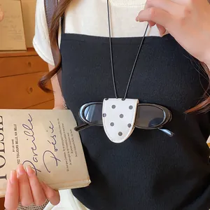Detail eines weißen gepunkteten Brillenclip-Anhängers aus Leder auf einem Pullover