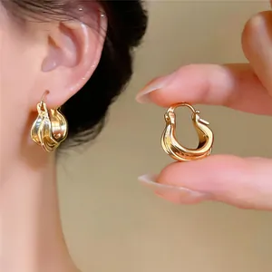 Elegante goldene gedrehte Creolen im Detail am Ohr getragen und in der Hand gehalten