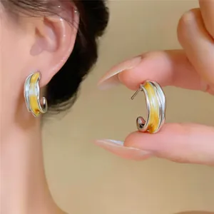 Detailaufnahme eleganter silberfarbener Creolen mit gelben Farbakzenten und edlem Design