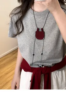 Nahaufnahme einer Halskette mit rotem kreisförmigem Anhänger auf einem grauen T-Shirt.