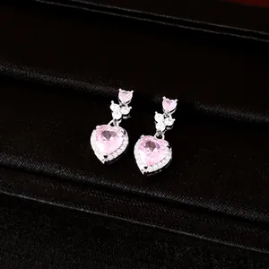 Close-up van elegante zilveren oorbellen met roze hartvormige zirkonia's en kristallen.