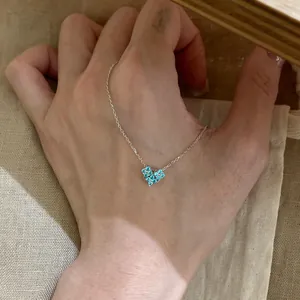 Detailed view of sparkly blue zircon heart pendant necklace with silver chain on hand.