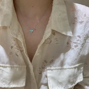 Detail of a delicate silver necklace with light blue zircon heart pendant on model.