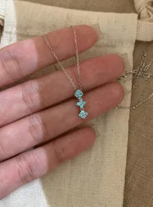 Detail view of shimmering blue zircon flower pendant necklace held on hand for scale