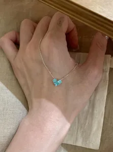 Detailed view of a silver heart necklace with blue zircons displayed on a hand