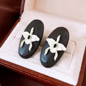 Close-up van ovale houten oorknopjes met een witte orchidee en een zwarte edelsteen