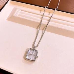 Dettaglio di un ciondolo orologio quadrato in argento su una catena in un vassoio.