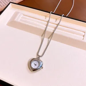 Dettaglio di una collana con orologio da taschino a cuore argento in un vassoio portagioie.