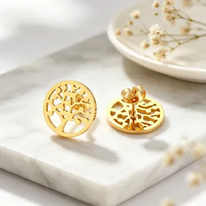 Détail macro de boucles d'oreilles arbre de vie en acier titane doré sur du marbre blanc