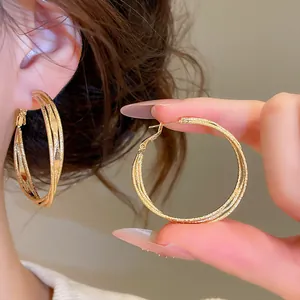 Detailed view of triple-layer twisted gold hoop earrings with shimmering textured finish.