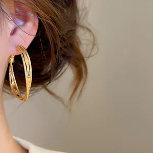 Detailed view of gold triple-layered twisted hoop earrings worn on model's ear.