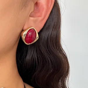 Nahaufnahme eines goldenen Retro-Ohrsteckers mit rotem Marmor-Acrylstein am Modellohr.