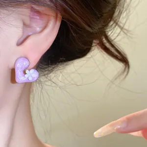 Detailed view of a purple resin heart earring with a small white flower on a model's ear.