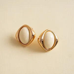 Makro-Detail von Retro-Ohrsteckern mit cremefarbenem Acryl-Oval und Gold-Finish