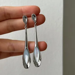 Vue détaillée de boucles d'oreilles pendantes minimalistes avec pierres œil-de-chat blanches.