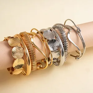 Detailopname van zes geometrische metalen armbanden met geplooide afwerkingen.