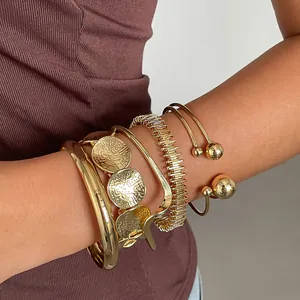 Gedetailleerd overzicht van zes gestapelde goudkleurige geometrische metalen armbanden.